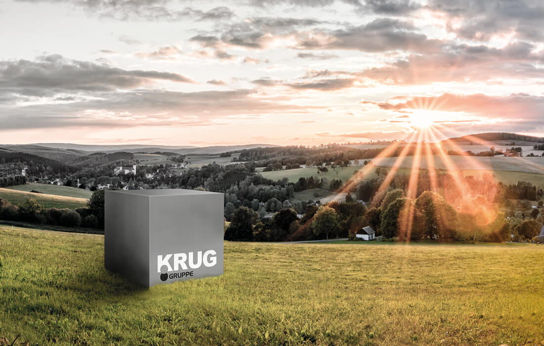 Das KRUG-Logo auf einem Würfel, der auf einer Wiese steht, vor dem Sunnenaufgang.